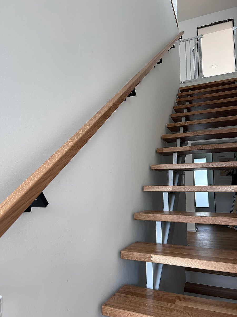 Offene Treppe mit Eichenstufen und weißen Wangen, an der Wand ein Eichenhandlauf auf schwarzen Haltern