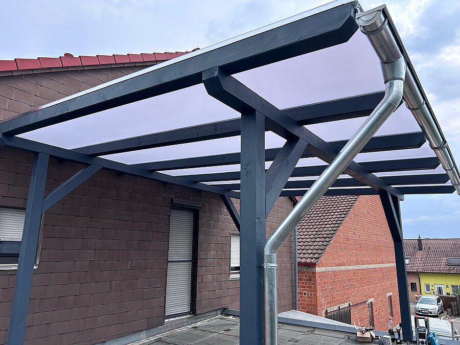 Carport mit anthrazitfarbenem Holzgerüst und lichtdurchlässigem Dach an einer Hauswand