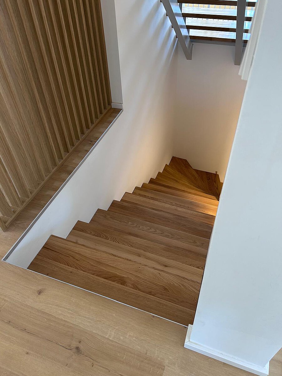Blick von oben auf eine gewendelte Eichentreppe, links eine Wandverkleidung aus senkrechten Holzlamellen