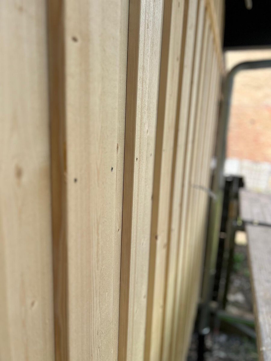Kante einer neuen Holzfassade aus senkrechten, unbehandelten Latten