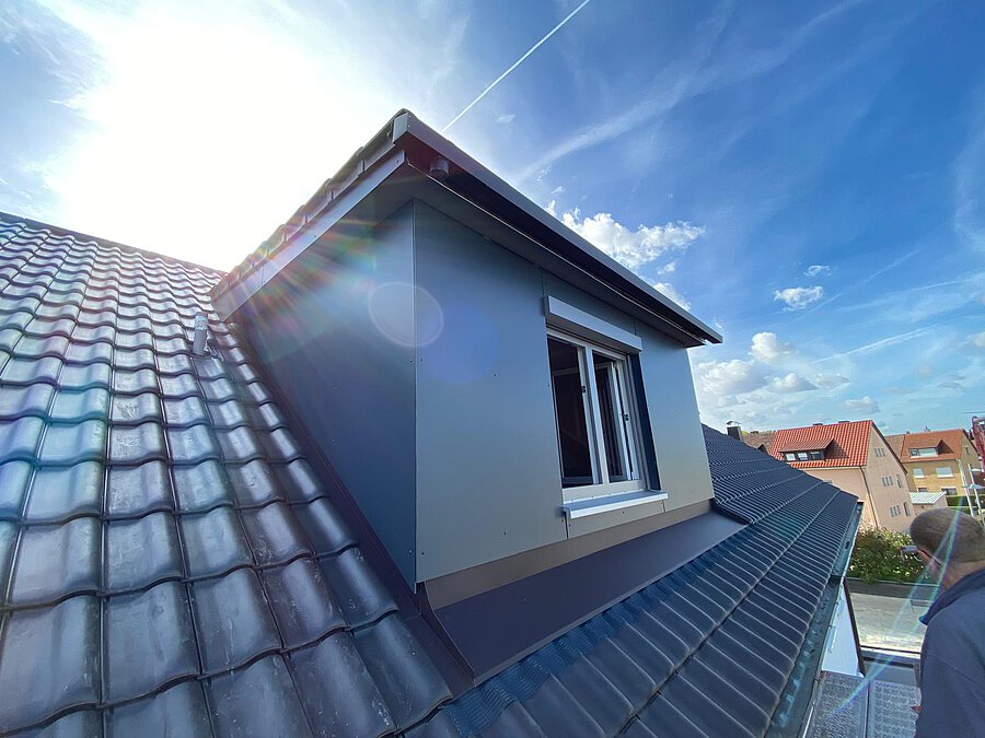 Neu verkleidete Dachgaube mit grauer Front und weißem Fenster, ringsum anthrazitfarbene Dachziegel
