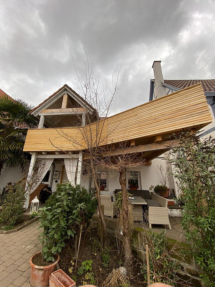 Überdachte Terrasse mit heller Holzverkleidung an der Dachunterseite, davor Gartenmöbel